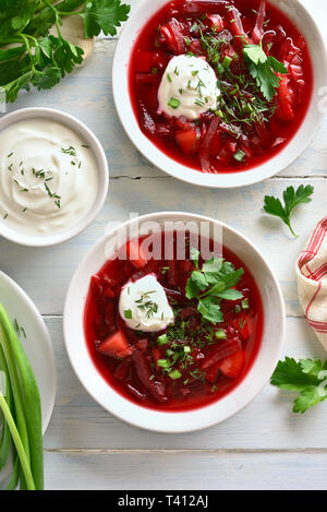 Lecker Rote-Bete-Suppe in Schüssel auf weiße Holztisch. Traditionelle Ukrainisch Russisch-Suppe (Borschtsch) mit grünen und Sauerrahm. Ansicht von oben, flach Stockfoto