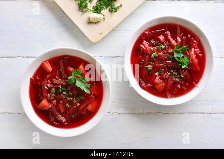 Rote-bete-Suppe in der Schüssel auf weißem Holz- Hintergrund. Traditionelle Ukrainisch Russisch-Suppe (Borschtsch) mit den Gruenen. Ansicht von oben, flach Stockfoto