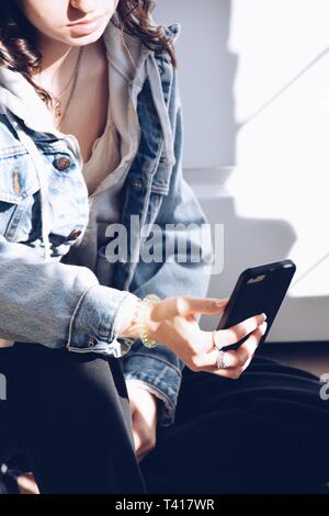 Junges Mädchen sitzt auf dem Boden mit einem Mobiltelefon Stockfoto