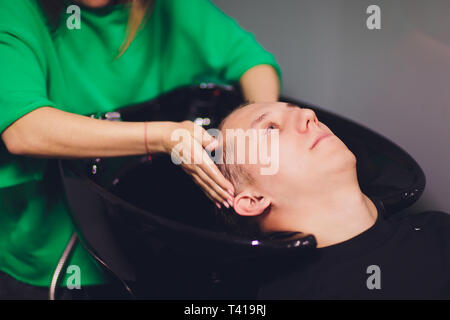 Junger Mann wäscht seinen Kopf in einen Friseursalon. Stockfoto