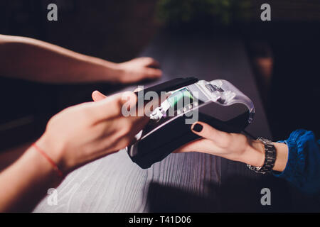 Zufrieden aussehenden bärtigen Mann in Ohrhörer mit Kreditkarte Kellnerin beim Zahlen für Rechnung im Cafe. Stockfoto