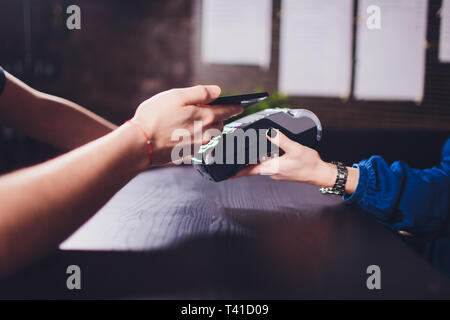 Zufrieden aussehenden bärtigen Mann in Ohrhörer mit Kreditkarte Kellnerin beim Zahlen für Rechnung im Cafe. Stockfoto