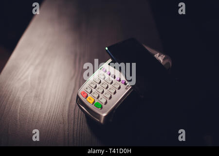 Zufrieden aussehenden bärtigen Mann in Ohrhörer mit Kreditkarte Kellnerin beim Zahlen für Rechnung im Cafe. Stockfoto