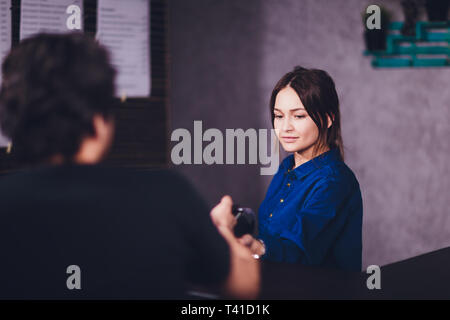 Zufrieden aussehenden bärtigen Mann in Ohrhörer mit Kreditkarte Kellnerin beim Zahlen für Rechnung im Cafe. Stockfoto