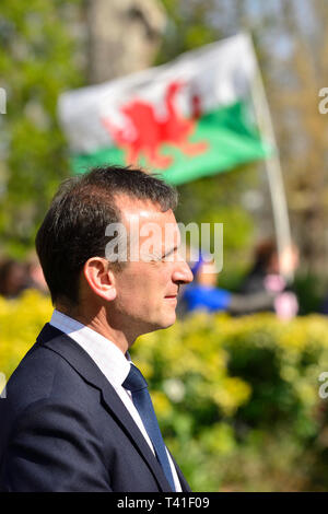 Alun Cairns MP (Con; Staatssekretär für Wales) auf College Green, Westminster, 11. April 2019 eine Flagge von Wales hinter, durchgeführt von einem Pro-EU-demonstrant ich Stockfoto