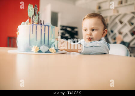 Toddler boy berührt Kuchen zum Geburtstag auf dem Tisch, die durch seine Hände. Stockfoto