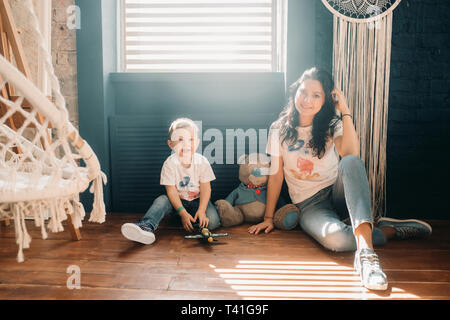 Die Mutter sitzt mit ihrem kleinen Sohn auf einem Stockwerk gegenüber dem Fenster. Stockfoto