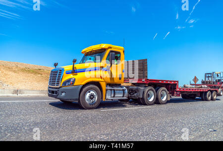 Gelb Big Rig Tag cab Semi Truck für lokale regionale Lieferung mit leeren Schritt nach unten Auflieger und Gabelstapler am Ende der Anhänger montiert läuft Stockfoto