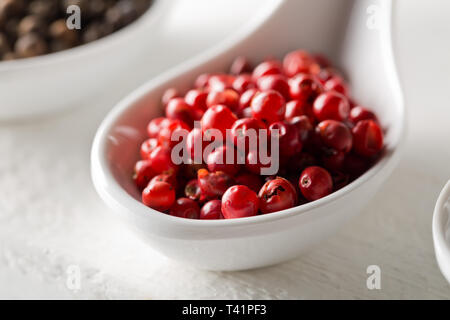 Pink oder Rosa brasilianischen roter Pfeffer (Schinus terebinthifolius) in Weiß Löffel auf weiße Holztisch Hintergrund - selektive Fokus Stockfoto