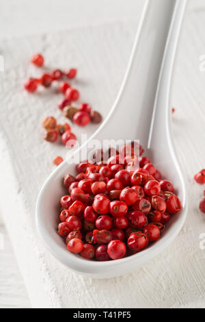 Pink oder Rosa brasilianischen roter Pfeffer (Schinus terebinthifolius) in Weiß Löffel auf weiße Holztisch Hintergrund - selektive Fokus Stockfoto