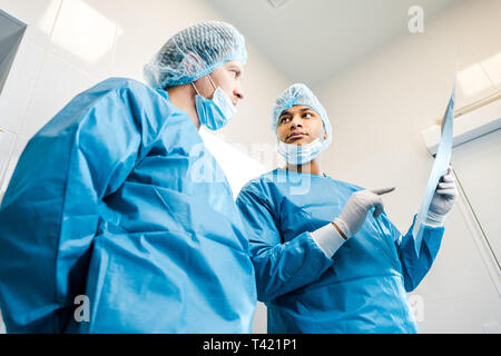 Low Angle View von stattlichen Ärzte in Uniformen und medizinische Masken sprechen über x-ray Stockfoto