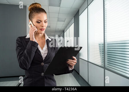 Hübsche Geschäftsfrau mit Zwischenablage Gespräche am Telefon in modernen Büro Stockfoto