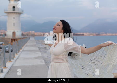 Portrait von wunderschönen, romantischen weiblichen ausgebreiteten Armen vor dem Leuchtturm posieren. Horizontale Komposition. Stockfoto