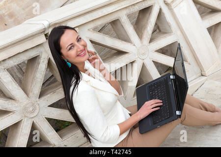 Elegante Frau im Gespräch mit Mobile beim Arbeiten mit Ihrem Laptop Stockfoto