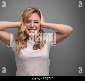 Attraktive Frau deckt Ihre Ohren mit den Händen auf einem grauen Hintergrund. Stockfoto