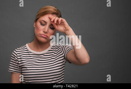 Müde Frau auf grauem Hintergrund. Die Blondine hält Ihren Kopf mit geschlossenen Augen. Stockfoto