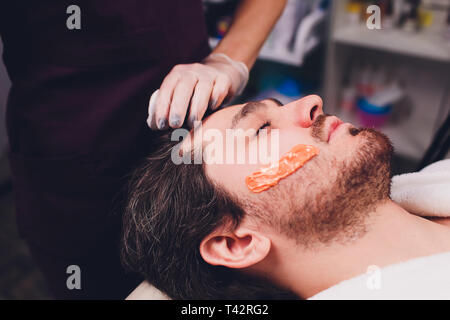 Haarentfernung. Der Mann Gesicht Zuckerpaste epilations Bartschneiden, gelbe Farbe, in der Kosmetik auf der Couch. Stockfoto