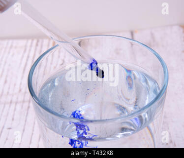 Drop blaue Flüssigkeit mit der Pipette in ein Glas mit Wasser Stockfoto