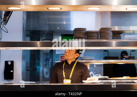 MANCHESTER, Großbritannien - 9 April 2019: ein Chef in einem Flughafen Küche schaut auf einen Bildschirm für die nächste Bestellung Stockfoto