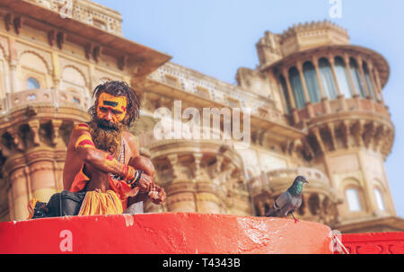 Sadhu Baba in Varanasi Ganges ghat mit alten Architektur Gebäude als Kulisse zu sitzen. Stockfoto