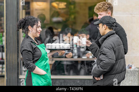 Eine weibliche Starbucks Mitarbeiter Hände warm Proben an die Öffentlichkeit in Prague Old Town Square Stockfoto