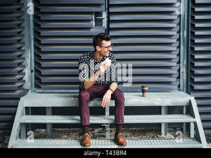 Ein junger Geschäftsmann mit Kaffee und Sandwich Sitzen im Freien, einen Snack. Stockfoto