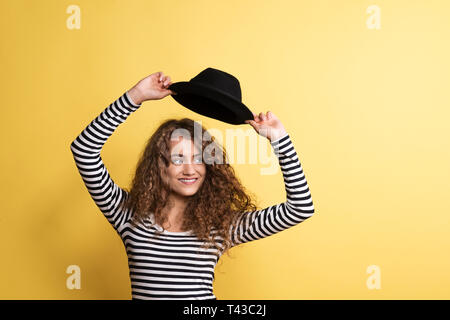 Porträt einer jungen Frau mit schwarzem Hut in einem Studio auf einem gelben Hintergrund. Stockfoto