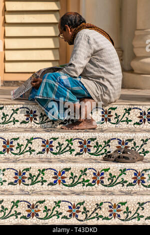 Vertikale Nahaufnahme von einem Mann beim Lesen einer Zeitung auf malerische Mosaiken in Kalkutta Jain Tempel in Kalkutta aka Kalkutta, Indien. Stockfoto