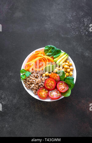 Buddha Schüssel Salat mit Buchweizen, Avocado, Karotten, Tomaten, Spinat, Kichererbsen auf Schwarz. Gesunde vegetarische vegane Ernährung Essen, super Essen. Ansicht von oben, cop Stockfoto
