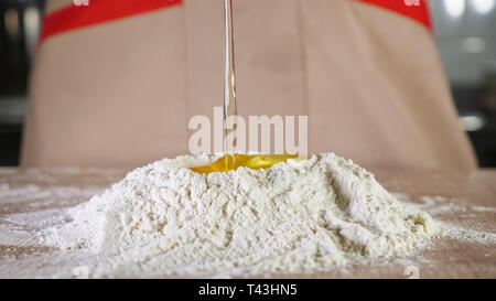 Baker ist das Hinzufügen von Ei zum Mehl einen Teig auf dem Tisch. Die Hände schließen. Stockfoto