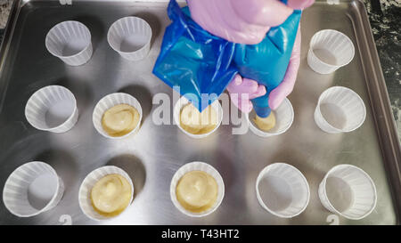 Konditor füllen Teig zum backen Muffins in Pappbechern auf einem Tablett mit spritzbeutel.. Close-up Hände. top View Stockfoto