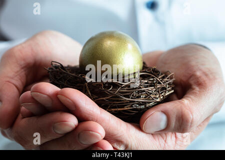 In der Nähe der menschlichen Hände, die goldene Eier in kleinen Nest Stockfoto