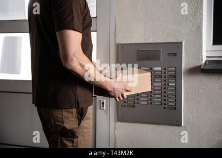 Im mittleren Abschnitt der Mann mit Karton Klingeln Intercom Stockfoto