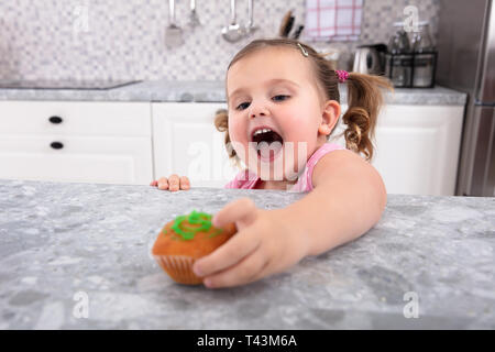 Lächelnd Cute Girl's Hand erreichen Für Cupcake auf den Küchentisch Stockfoto