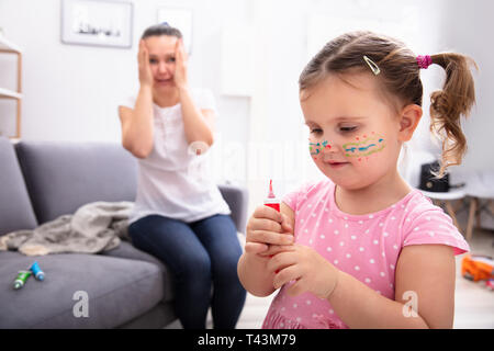 Schockiert Mutter sitzt auf einem Sofa mit Blick auf ihre Tochter Malerei Gesicht mit Farbe Rohr Stockfoto