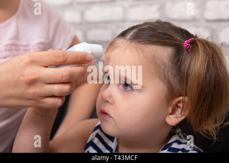 Mutter Kontrolle Fieber Ihrer kranken Tochter mit Stirnthermometer zu Hause Stockfoto