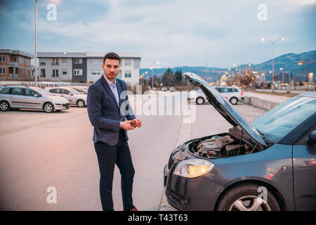 Einen müden Arbeiter steht neben seinem Auto formell gekleidet und Suchen über die Autos Motor Problem besorgt. Stockfoto