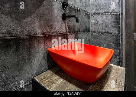 Roten Waschbecken mit Wasserhahn in teuren loft Bad in Elite Sport Bar auf schwarzen Mauer Hintergrund Stockfoto