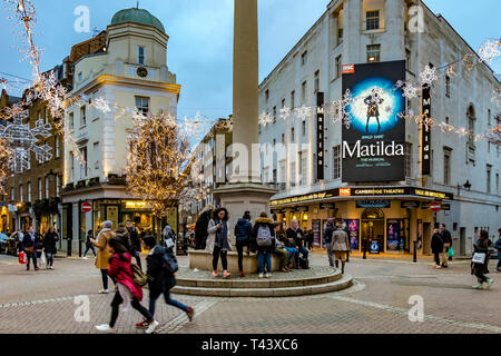 Weihnachtslichter im Seven Dials, beschäftigt mit Einkäufern und Besuchern, die am Cambridge Theatre vorbeilaufen und Matilda, das Musical, London, Großbritannien, zeigen Stockfoto