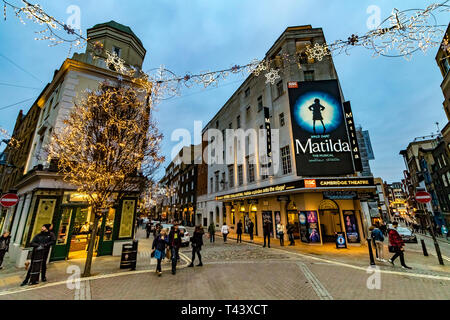 Weihnachtslichter im Seven Dials, beschäftigt mit Einkäufern und Besuchern, die am Cambridge Theatre vorbeilaufen und Matilda, das Musical, London, Großbritannien, zeigen Stockfoto