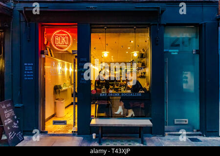 Eine Frau sitzt an einem Tisch am beleuchteten Fenster in Boki, einem unabhängigen Café in Seven Dials, London, Großbritannien Stockfoto