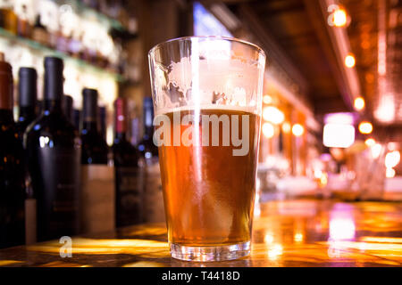 Glas Pint bernsteinfarbenes Bier mit bunten Unschärfe der Bar im Hintergrund Stockfoto