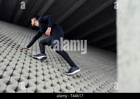 Sport mann Klettern im Beton graue Wand, und dabei seine Ausbildung im städtischen Bereich Landschaft. Konzept der Ziele und Erfolge im Sport erreichen. Stockfoto