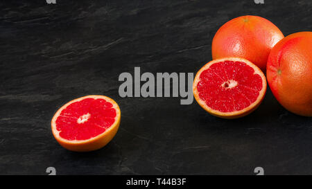 Rosa Grapefruits, eine Frucht halbiert, auf schwarzem Schiefer wie Vorstand, breiten Raum für Text, Foto, linke Seite Stockfoto