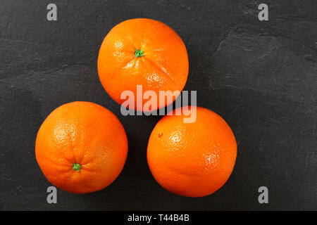 Ganze drei orange Zitrusfrüchte auf schwarzem Schiefer, Flachbild Foto legen Stockfoto