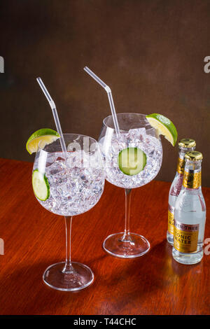 Gin und Tonic, modernen Stil-globe Glas, viel Eis, Scheiben Gurke und Kalk und einem Stroh Stockfoto