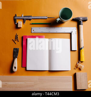 Workshop Szene. Zusammensetzung der Werkzeuge, Späne, Tasse, Bleistift und Notebook auf dem orange Tabelle Stockfoto