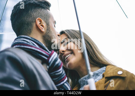 Glückliches Paar küssen unter einem Sonnenschirm an einem regnerischen Tag - schöner Mann küssen seine Stirn Freundin unter dem Regen - Liebe, Menschen, Beziehung Konzept Stockfoto