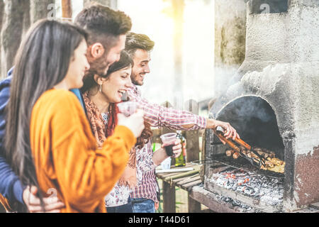 Jugendliche mit einem Grillfest im Hof auf dem Berg - glückliche Freunde Grillen von Fleisch und trinken Rotwein outdoor Stockfoto
