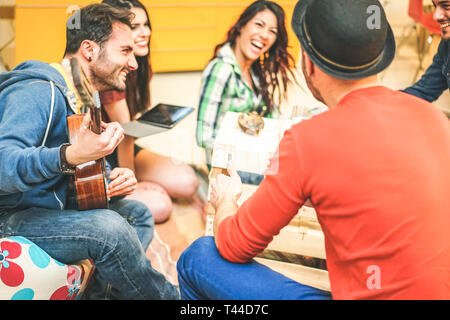 Gruppe von Freunden Spaß haben im Wohnzimmer in ihr Haus - Glückliche junge Menschen spielen Musik mit Gitarre und Gesang und zusammen lachen Tablet Stockfoto